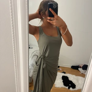 Grön ärmlös klänning - Snygg grön ärmlös klänning med knytning i midjan. Perfekt för en stilren och bekväm look. Klänningen har en smickrande passform och är gjord i ett mjukt material.