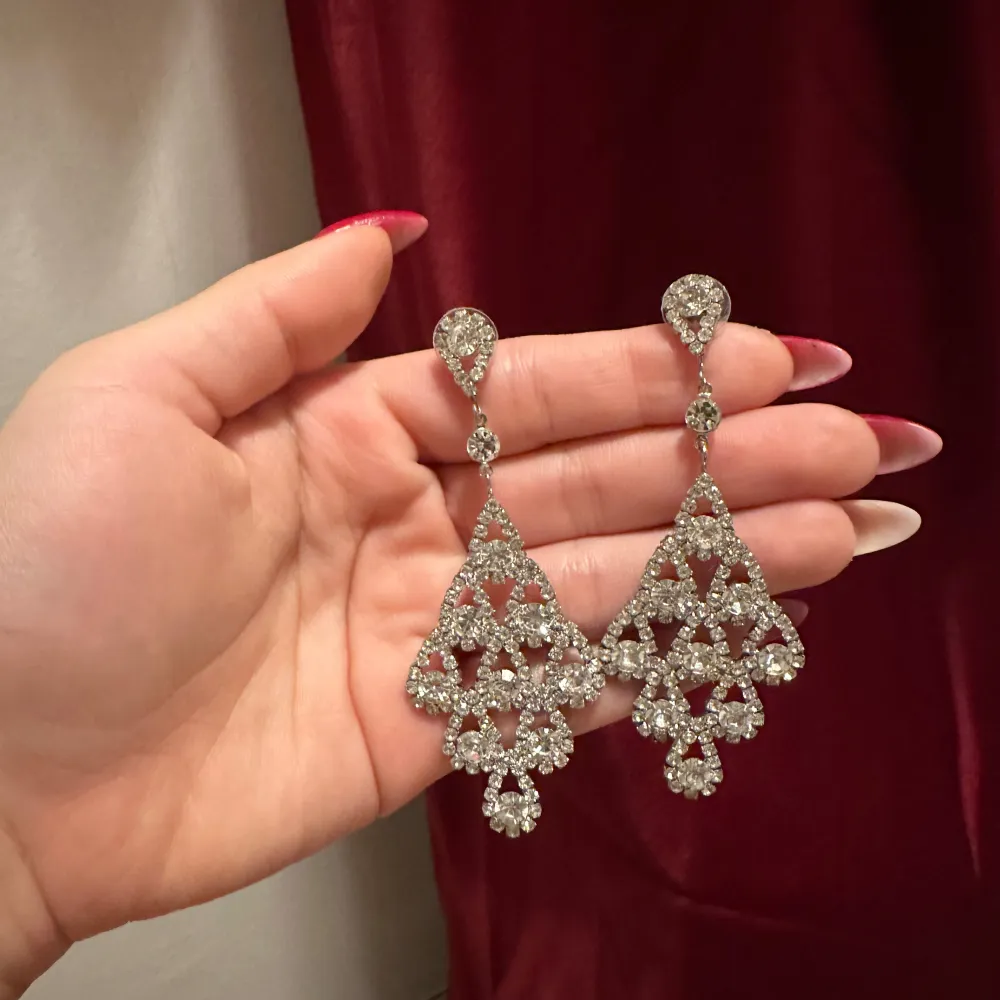 Säljer ett par fantastiska glittriga örhängen i silver. De har en triangulär form med flera små gnistrande stenar som ger en lyxig känsla. Perfekta för att lysa upp vilken outfit som helst.. Asusteet.