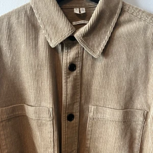 Beige manchester overshirt - Säljer en snygg beige manchester overshirt med knappar framtill. Den har en regular fit och två praktiska bröstfickor. Perfekt för lager-på-lager-stilen under höst och vår. Långärmad design med en stilren look.