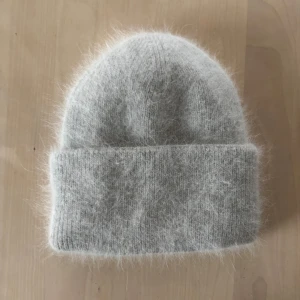 Grå fluffig mössa från BUON - Helt ny mysig grå mössa från BUON i ett fluffigt pälsmaterial. Perfekt för att hålla värmen under kyliga dagar. Den har en enkel design med uppvikt kant för extra stil och komfort.🩷