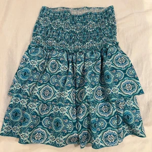 Mönstrad blå kjol - Snygg blå kjol med ett detaljerat mönster i olika nyanser av blått och vitt. Kjolen har en elastisk midja och volanger som ger en fin form. Perfekt för en somrig look!