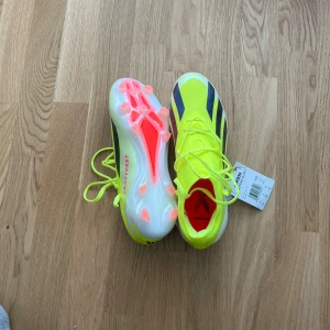 fotbollsskor - Snygga neongula fotbollsskor från Adidas med svarta detaljer och snörning. Skorna har en vit sula med rosa dobbar, perfekt för att dominera på planen. De är designade för att ge bra grepp och snabbhet. Helt nya oanvända, köpt för 2499kr