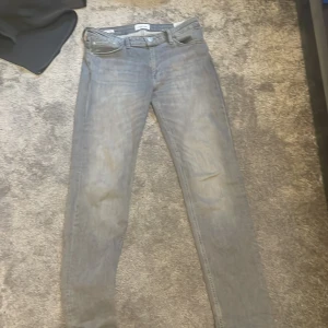 Grå jeans från Jack & Jones - Säljer ett par grå jeans från Jack & Jones, modell Regular/Clark. De har en klassisk femficksdesign och en knappgylf. Perfekta för en avslappnad stil. Bra skick, inte så använd, storlek 30 Bredd 34 längd.