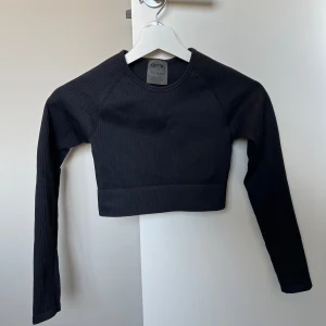 Svart ribbad croppad tröja från Aim'n - Säljer en svart ribbad croppad tröja från Aim'n. Tröjan har långa ärmar och ett mjukt och stretchigt material. Perfekt för träning eller till vardags.