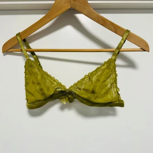 Olivgrön spets-bh från H&M - Säljer en olivgrön spets-bh från H&M med en söt rosett framtill. Bh:n har justerbara axelband och är tillverkad i ett fint spetsmaterial som ger en elegant look. Perfekt för att känna sig extra fin under kläderna. 💚