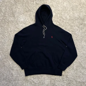 Ralph Lauren Hoodie - Snygg mörkblå hoodie från Ralph Lauren, hoodien har ett rött Ralph Lauren märke på bröstet och vita snören. Storlek M. Skick 8,5/10 Hör gärna av dig vid frågor!