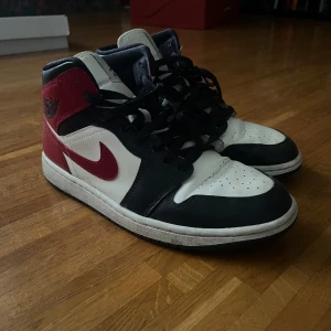 Nike Air Jordans i svart, vitt och rött - Säljer ett par klassiska Nike Air Jordans i svart, vitt och rött. Skorna har en mid modell med snörning och den ikoniska Nike-loggan på sidan. Perfekta för dig som älskar sneakers med stil och komfort.