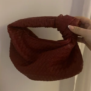 Röd flätad handväska - Snygg röd handväska med flätat mönster. Väskan har en unik design med en vriden topp. Den har aldrig använts och är som ny, köpt för ca 6 månader sen.