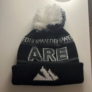 Åre mössa - Snygg svart mössa med stor tofs och texten 'SWEDEN' samt 'ÅRE' i vitt. Mössan har ett bergsmotiv framtill och ribbad kant. Perfekt för kalla dagar. Använd få tal gånger köpte den i Åre för några veckor sedan, kommer inte till användning pris kan diskuteras.