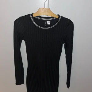Svart ribbad klänning  - Snygg svart ribbad klänning från Divided med långärmad design. Perfekt för nyår eller fest. Klänningen har en tajt modell med vita detaljer. Använd fåtal gånger skriv för fler bilder 
