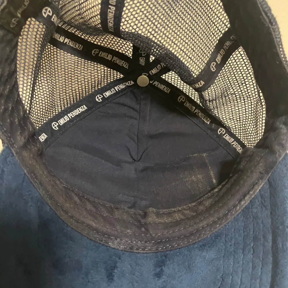 Snygg blå keps från Emilio Pendenza med ett unikt tryck av en strandscen på framsidan. Kepsen har ett nätmaterial på baksidan för bättre ventilation. Perfekt för en avslappnad stil.. Asusteet.