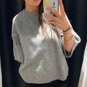 Grå stickad tröja - Säljer en stilren grå stickad tröja med trekvartsärm.  Tröjan har en rund halsringning och en avslappnad passform.