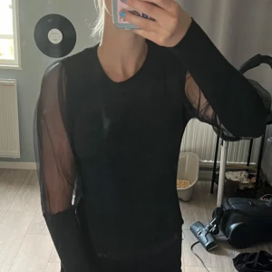 Svart långärmad topp med transparenta ärmar - Snygg svart topp med långärmade transparenta ärmar. Perfekt för en stilren look. Passar bra till både jeans och kjol.
