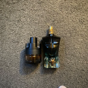 Två parfymer i unika flaskor - Säljer två parfymer med unika flaskor. Den ena har en mörk, rund flaska med svart lock och texturerad yta. Den andra är formad som en torso i mörkblått glas med en guldig spraytopp. Perfekt för den som vill ha något speciellt i sin samling.