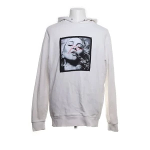 Vit hoodie från Kissing The War - Säljer en vit hoodie från Kissing The War med ett tryck av en kvinna på framsidan och text på baksidan. Tillverkad i 100% bomull och har långa ärmar samt en klassisk huva. Perfekt för en avslappnad stil.