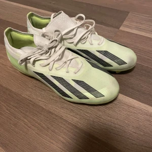 Fotbollsskor från Adidas modell PRO  - Snygga fotbollsskor från Adidas i en fräsch vit och limegrön färgkombination. Skorna har snörning och en modern design med svarta detaljer på sidan. Perfekta för fotbollsplanen med en greppvänlig sula.