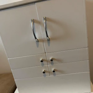Vit sminkskåp med spegel - Praktiskt och stilrent vitt  Sminkskåpmed flera fack och lådor för optimal förvaring. Utrustat med en spegel på insidan av locket och svarta insidor för en elegant kontrast. Perfekt för att organisera smink och accessoarer.