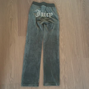 Juicy Couture velourbyxor grå XXS - Mörkgrå velourbyxor från Juicy Couture med strassdetaljer och texten 'Juicy' på baksidan. Byxorna har resår och snörning i midjan samt raka ben. Klassisk logga framtill och mjukt material som ger en chill vibe. Köpt för 1000 kr och säljs nu för 500 kr. Dessa mjukisbyxor har används en eller några fåtal gånger.