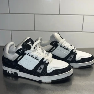 Louis Vuitton trainers sneakers svart/vit - Storlek 45! Snygga Louis Vuitton sneakers i svart och vitt med klassiskt monogrammönster. Skorna har rund tå, platt sula och vita snören. Materialmix av skinn och textil med tydliga LV-detaljer på tunga och häl. Perfekta för dig som vill sticka ut med lyxig streetstyle.