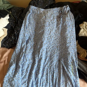 Blommig blå långkjol från New Look - Supersöt blå långkjol från New Look med små vita blommor och svarta detaljer. Kjolen har omlottknytning i midjan och är perfekt för en chill och somrig vibe. Lätt och flowy känsla, passar perfekt till sneakers eller sandaler.obs har fläck