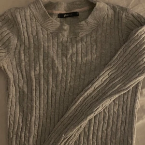 Ljusgrå kabelstickad tröja Gina Tricot - Superskön ljusgrå kabelstickad tröja från Gina Tricot. Klassisk rund halsringning och långa ärmar. Perfekt för lager-på-lager och enkel att matcha med jeans eller kjol. Mjuk och stretchig känsla som gör den extra bekväm. FLÄCK (Bild 2)