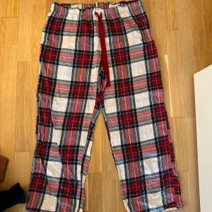 Rutig pyjamasbyxa från H&M, storlek L - Säljer ett par rutiga pyjamasbyxor från H&M i storlek L. Byxorna har röd, vit och grå färg, elastisk midja med snörning och är tillverkade i mjuk bomull. Perfekta för chill hemma eller mysiga kvällar.