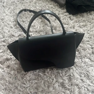 Svart ATP väska - Stilren svart handväska från ATP! Detta är den stora modellen. Använd men fortfarande i väldigt bra skick! 🩷🩷 Kvitto saknas då den är köpt här på Plick, men dustbag tillkommer. Skriv vid intresse! 