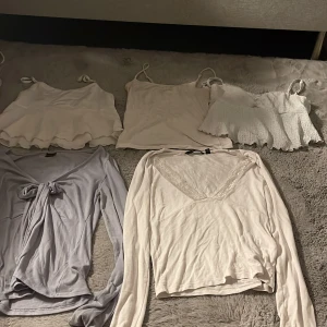 Fem toppar i ljusa toner, blandade modeller - Säljer fem olika toppar i ljusa färger. Tre ärmlösa linnetoppar med smala axelband, varav en har volangkant och en är smockad. Två långärmade toppar, en omlottmodell i ljusgrått med knyt och en vit med spetsdetalj vid v-ringningen. Perfekt för att mixa och matcha. Säljer alla för 100kr annars 25kr styck 💕
