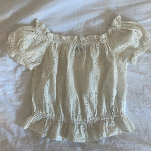 Vit blus  - Supersöt vit blus med broderade blommor och volangkant. Offshoulder-modell med korta puffärmar och resår vid hals och midja. Perfekt sommarkänsla 🩷🌸kontakta för mer info och intresse 