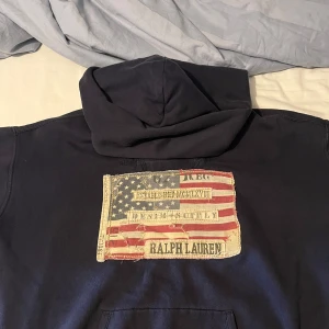Mörkblå hoodie från Ralph Lauren - Snygg mörkblå hoodie från Ralph Lauren med stor patch på ryggen som har amerikansk flagga. Har nästan aldrig använt 