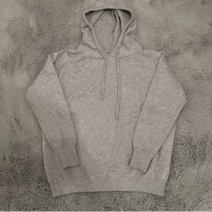 Grå merinoull hoodie med huva - Mysig grå merinoull hoodie med huva och snörning. Tröjan har långa ärmar, ribbade muddar och en klassisk passform. Perfekt för dig som gillar en enkel och stilren look med en soft vibe.