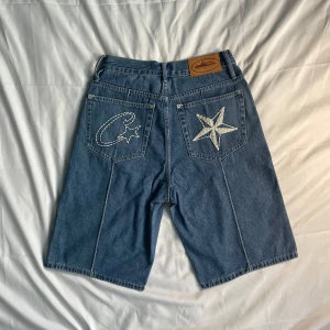 Corteiz Jeans Short - Corteiz Denimshorts – Storlek S – Helt nya  🆕 Skick: Helt nya, aldrig använda 📏 Storlek: S (Small) 👖 Färg: Klassisk blå denim 🌟 Design: Ikonisk Corteiz Alcatraz-lapp på midjebandet med djärv broderad grafik – stjärna + halvmåne "C" på ena fickan och stor stjärna på den andra. Unik, framträdande Corteiz-look.  🔗 Detaljer: Kraftig, högkvalitativ denim med signatur streetwear-styling. Perfekt för sommarkläder eller att bära med Corteiz-essentials.  🔥 Sällsynt dropp – köp den innan den är slut! 