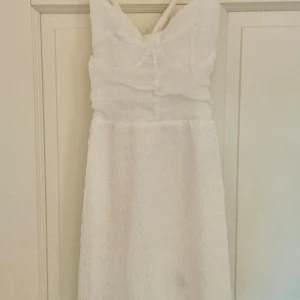 Vit sommarklänning från H&M Divided - Superfin vit klänning från H&M Divided med korsade axelband och snörning i ryggen. Lätt och luftig modell i bomull, perfekt för varma dagar. Klänningen är ärmlös och har en kort längd som ger en fräsch och trendig look. Öppen för bud vid snabbaffär!