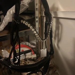 Svart träns ponny med glittriga stenar - Snyggt svart träns i ponny-storlek med ett pannband dekorerat med stora glittriga stenar. Har tyvärr inte kommit till användning därför sitter även prislappen kvar. Köpt från Ullared så minns inte pris men oanvänt. 