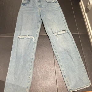 Ljusblå straight jeans med hål - Säljer ett par ljusblå straight fit jeans med hög midja och slitna hål över knäna. 