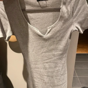 Grå  kortklänning med v-ringning - En enkel och stilren grå  kortklänning med v-ringad hals och korta ärmar. Perfekt för dig som gillar en clean och avslappnad look. Sitter snyggt och är lätt att matcha med sneakers eller boots.