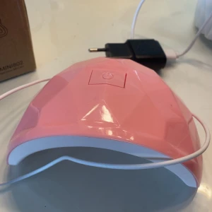 Rosa UV LED-lampa för naglar - Säljer en rosa UV LED-lampa för naglar, perfekt för gel- och shellacmanikyr hemma. Lampan har en snygg diamantformad design, USB-sladd och strömadapter medföljer. Enkel att använda med en stor power-knapp på ovansidan. Bara testad