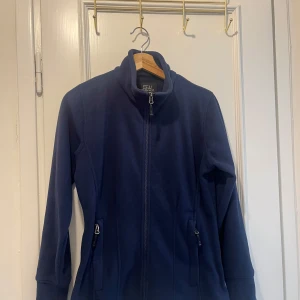 Mörkblå fleecejacka från South West från Vårdväska  - Mysig mörkblå fleecejacka från South West med hel dragkedja och höga fickor med dragkedja. Jackan har en enkel, stilren design med hög krage och lång ärm. Perfekt för kyliga dagar när du vill vara både bekväm och snygg. Använt några av enstaka gånger! 😊