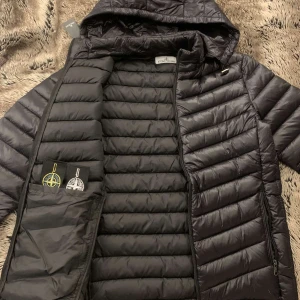 Stone Island jacket - Svart Stone Island jacka i storlek M med originella och Stvart vit badge, jackan är en tun puffer jacket och är perfekt för sommaren☀️, våren, hösten. Den är i helt perfekt skick och aldrig använts då den är för försäljning . Finns tags 🏷️ , 2️⃣ Stone Island badge, luvan är avtagbar för de som föredrar det, Certil logo QR Scan✅. Priset är inte hugget i sten och kan diskuteras🪨⛏️                                       Frågor och behov om mer bilder?  Kontakt mig🫡
