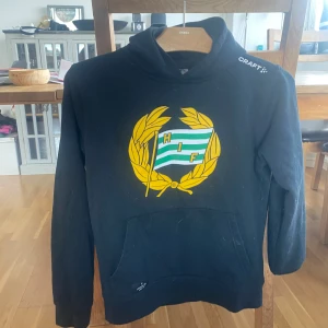 Svart HIF hoodie från Craft 158/164 - Svart hoodie från Craft med Hammarby IF-logga i gult och grönt framtill. Klassisk känguruficka och huva. Perfekt för dig som vill visa ditt stöd för Bajen. Skön passform och mjukt material. OBS: Pris kan diskuteras💕