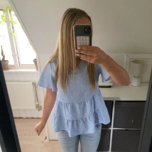 Blårandig volangblus från SHEIN - Supersöt blus från SHEIN i blåvitt randigt med v-ringning och volanger nertill. Korta ärmar och luftig passform, perfekt för varma dagar. Tillverkad i lätt bomullsmix som känns skön mot huden. Passar till jeans eller kjol för en fräsch look.