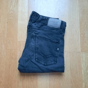 Svarta Replay jeans  - Säljer ett par mörkgrå jeans från Replay med klassisk femficksdesign. Jeansen har snygga detaljer på bakfickorna och en diskret Replay-logga. Tillverkade i mjukt denimtyg som sitter skönt hela dagen. Byxornas midja är 40cm och deras längd är 96 cm