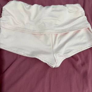 Vita högmidjade shorts i syntet - Snygga vita högmidjade shorts med bred linning och kort passform. Tillverkade i ett mjukt och stretchigt syntetmaterial som sitter bekvämt och följsamt. Perfekta för dig som gillar en clean och enkel look.