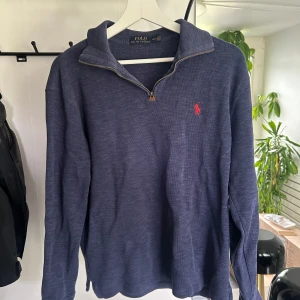 Blå half zip tröja från Polo Ralph Lauren - Mörkblå långärmad tröja från Polo Ralph Lauren med half zip och klassisk krage. Tröjan har röd broderad logga på bröstet. Tröjan har slitage på armbågarna (Se sista två bilderna), men är annars i bra skick.