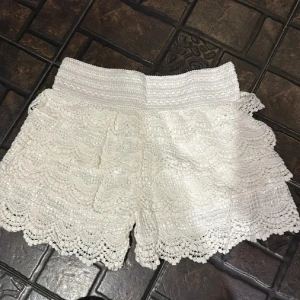 Vita spetsiga shorts med volang - Superfina vita shorts med bred resår i midjan och flera lager spets med volangkant. Perfekta för sommaren när du vill ha en romantisk och söt look. De har en feminin känsla och är riktigt bekväma att bära.