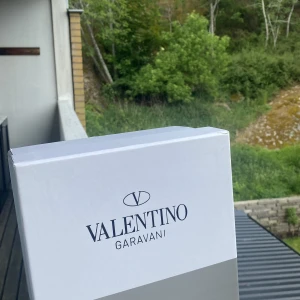 Valentino Garavani Open sneakers vit/svart - Snygga Valentino Garavani Open sneakers i vitt skinn med bred svart läderdetalj över sidan. Klassisk rund tå, vita snören och ikoniska nitar baktill på sulan. Perfekta för dig som vill ha en clean men lyxig look.