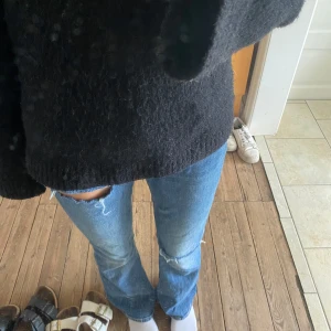 Blå bootcut jeans med slitningar - Säljer ett par jättesnygga blå jeans med bootcut passform och slitna detaljer vid knäna. Jeansen har klassisk femficksdesign med en normal midja. Perfekta för dig som gillar en avslappnad och trendig look🥰🥰 