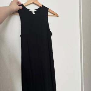 Svart ärmlös klänning H&M - En stilren svart ärmlös klänning från H&M med rund halsringning. Klänningen har en rak och enkel passform som ger en clean look. Perfekt att styla med sneakers eller boots för en cool vibe.