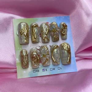 GLD3N (S);Medium Square - Snygga gelé press on-naglar i storlek S: 15 mm, 11,5 mm, 12 mm, 11 mm, 9 mm , med skimrande guldmönster och 3D-blommor. Basen är ljus och glittrig, dekorerad med swirliga gulddetaljer och pärlliknande blommor. 