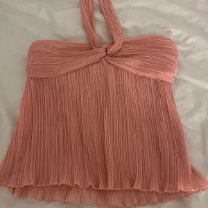 Plisserad rosa halterneck topp - Supersöt plisserad topp i ljusrosa med halterneck och twistad detalj framtill. Luftig och flowy modell som ger en riktigt somrig vibe. Perfekt till jeans eller kjol för en trendig look. Säljer du den är för stor för mig och inte kommer till användning. Är XS men liknar mer en S